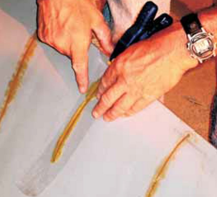 Stan running tape over freshly glued cracks in the Royalex canoe to prevent the glue from running and keep it relatively smooth when cured. Note: Use of simple spring clamp to keep the top edge of the Royalex aligned. (Always wear gloves when handling uncured epoxy—Ed.)