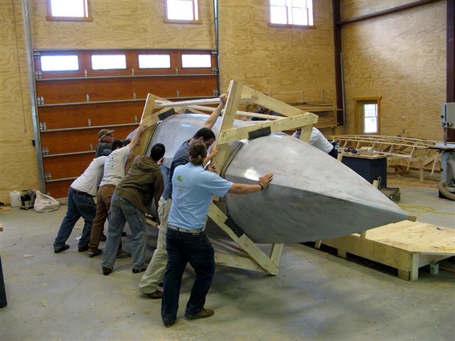 Advanced boatbuilding course students roll the hull over.
