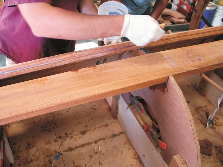Applying glue to the face and groove of one of the staves. When in place the brackets will be secured over the frame, and wedges forced between the frame and the stave will hold the stave tight against the bulkhead.