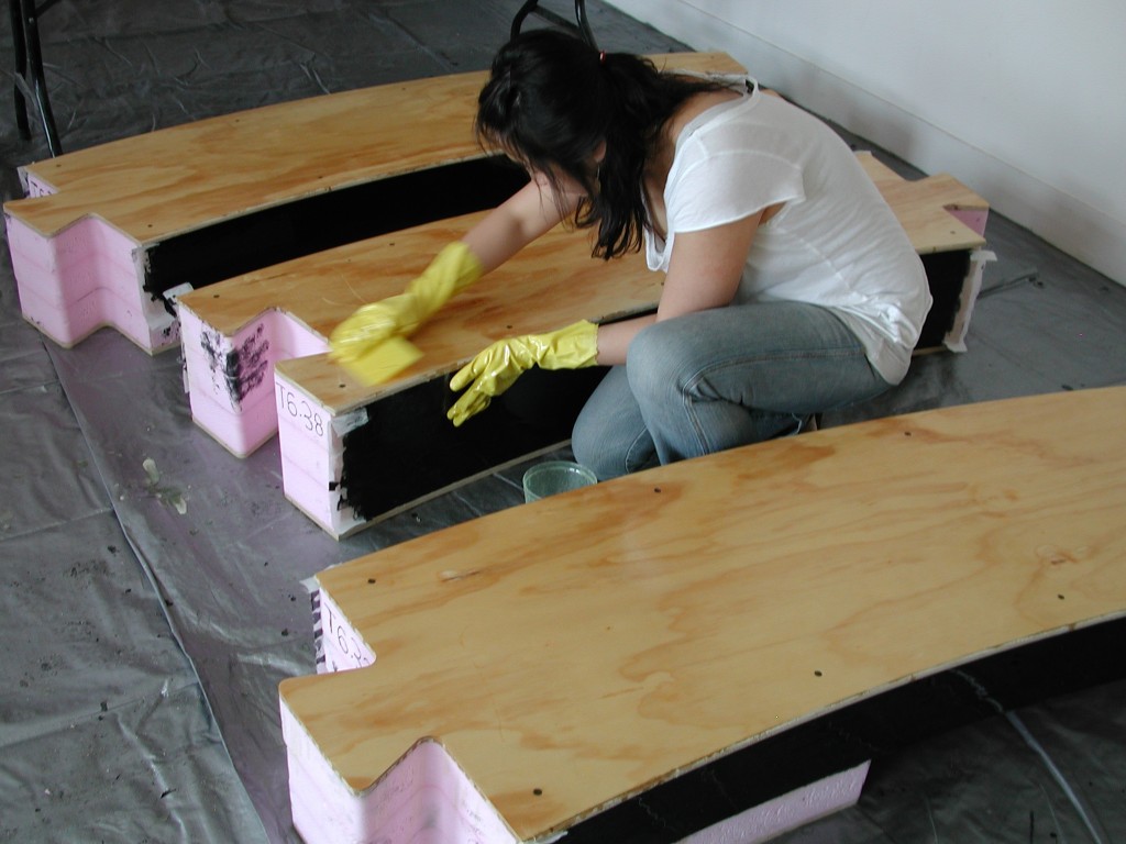 A worker coats one of the interlocking sections that make up the sides of one of the pools. The sections are laminated foam and wood.