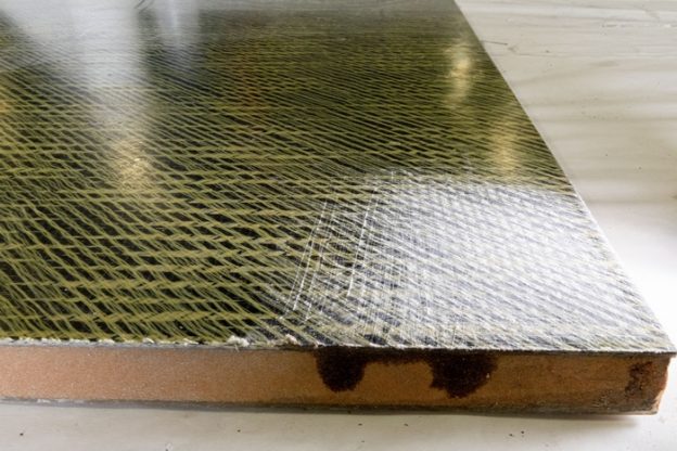Sample of a carbon fiber/Kevlar laminate affected by abrasion. The left side is unaffected where as the right side has been abraded. Note the fraying from the Kevlar fibers.
